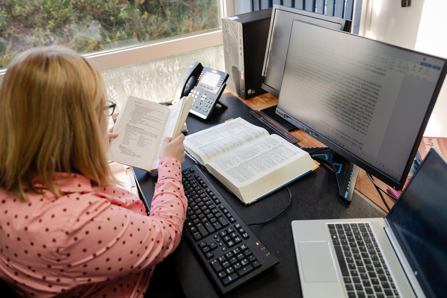 Member of Books Council staff at work at her computer, and using reference book.